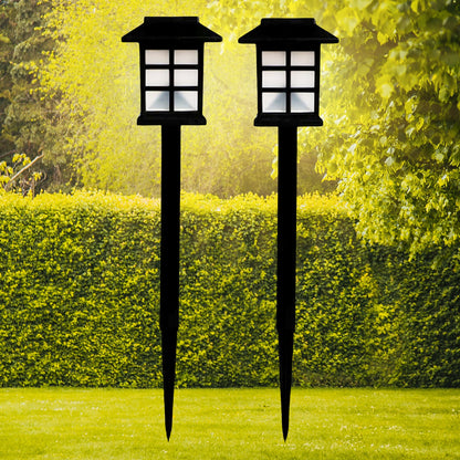 Two black solar garden lights with white paneled tops stand in a vibrant green lawn with hedges and trees.