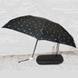 A black DrizzlePro umbrella with small gold musical note patterns is open next to its black zippered case on a sketched
