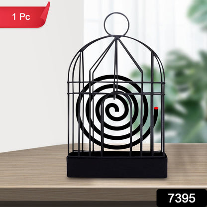 A black iron birdcage-style holder with a burning mosquito coil is on a wooden table, with a red