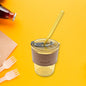 Clear glass coffee mug with lid and reusable straw, ideal for travel.