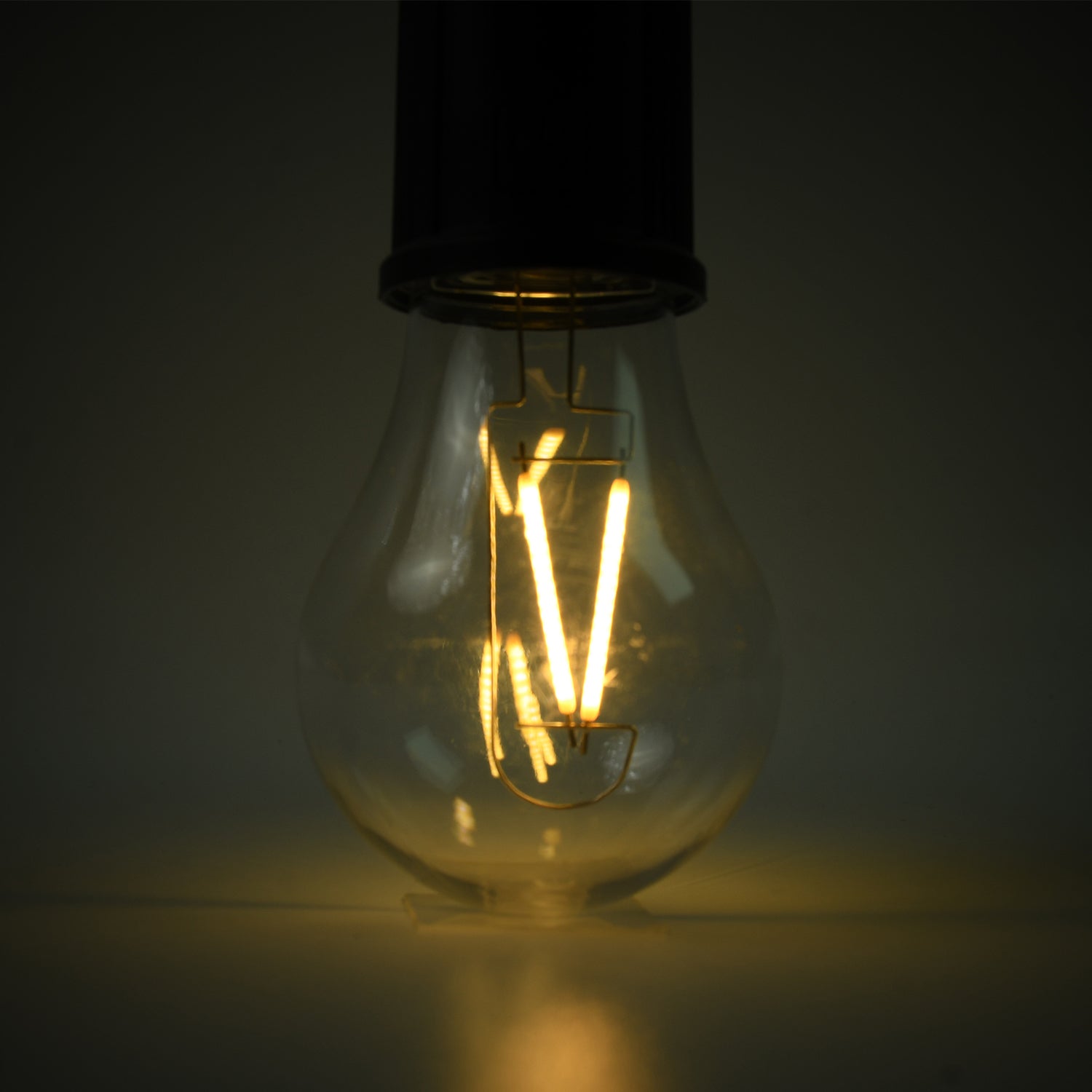 A close-up of the clear bulb of a portable LED tent light shows the glowing orange filament against a dark background.
