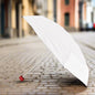 A white umbrella with a red handle stands open on a cobblestone street, ready for use.
