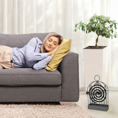 A black iron birdcage-style holder with a mosquito coil sits on a rug next to a gray sofa where a person is sleeping.