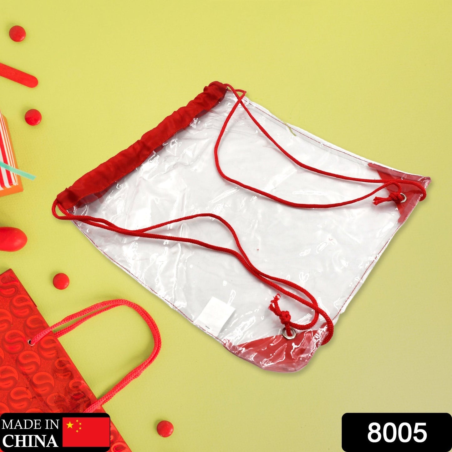 A clear drawstring bag with red accents is placed on a bright yellow surface, surrounded by red decorative items and a red
