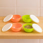 Set of four small round plastic bowls with clear lids for food storage.