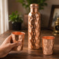 Diamond cut copper water bottle set with two matching glasses on a light background.