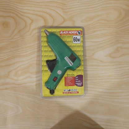 A green 60 Watt hot melt glue gun on a workbench, surrounded by crafting materials and tools.
