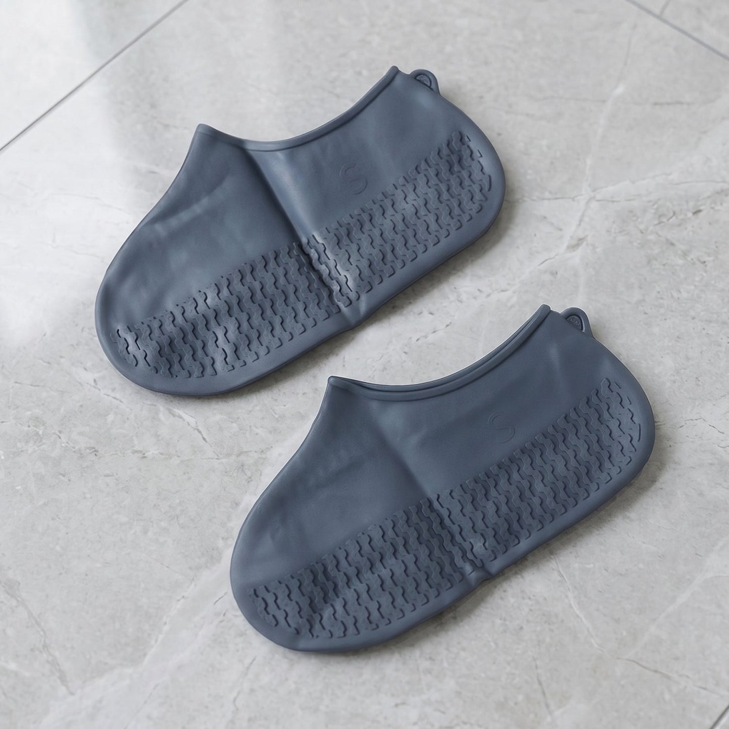 A pair of gray silicone foot coverings with textured soles rests on a light gray tiled surface.