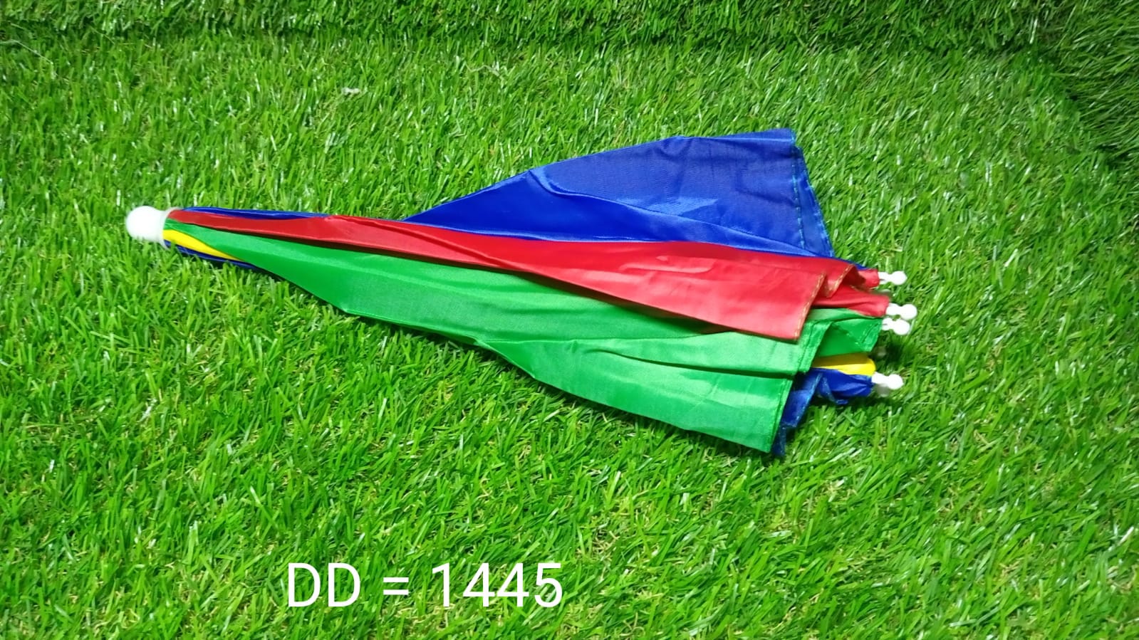 A folded, colorful red, yellow, green, and blue umbrella hat lies on vibrant green artificial grass.